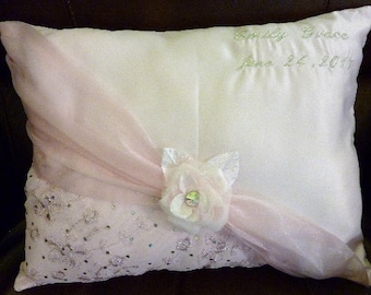May include: A white satin pillow with a pink sheer overlay and a lace trim. The pillow has the text "Emily Grace June 24, 2017" embroidered on it.