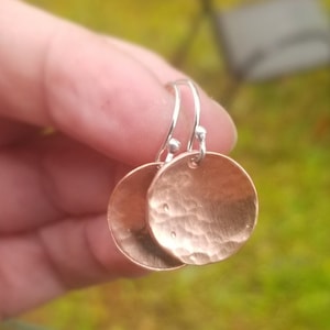 May include: A pair of hammered copper earrings with silver hooks. The earrings are round and have a textured surface.
