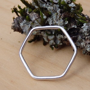 May include: A silver hexagonal ring, shown on a wooden surface with moss.