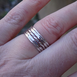 May include: A set of five silver stacking rings. The rings are all different widths and have a hammered texture.