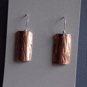 May include: A pair of copper earrings with a textured surface and silver hooks.