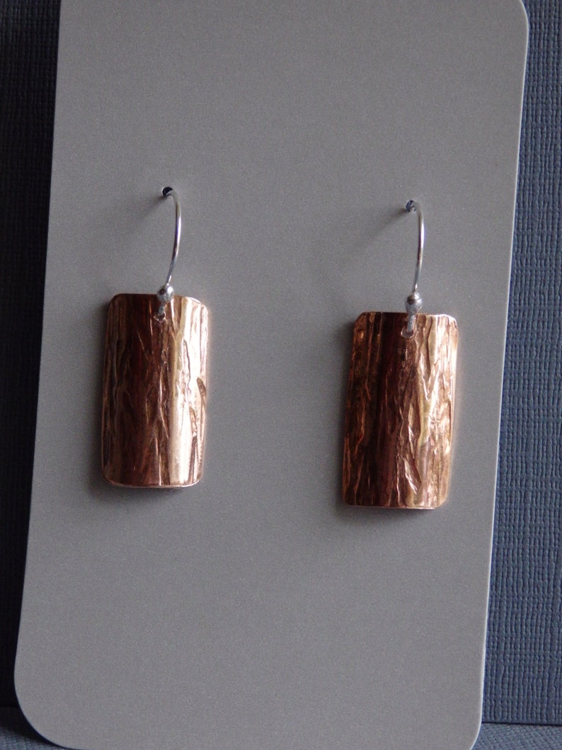 May include: A pair of copper earrings with a textured surface and silver hooks.
