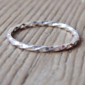 May include: A thin, circular ring crafted from polished silver metal. The band features a continuous, repeating twisted or spiralled texture throughout its entire circumference, creating a series of small, reflective facets that catch the light.