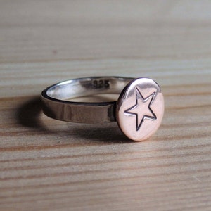 May include: A silver ring with a rose gold star-shaped disc. The ring is marked with "925" on the inside.