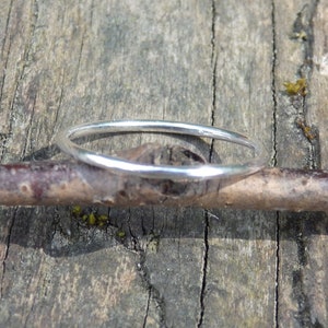 May include: A slender silver ring sits on a brown twig, with a background of aged wood. The ring's polished surface reflects light, giving it a gentle gleam. The natural setting accentuates the ring's understated charm.