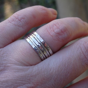 May include: A set of four silver hammered stacking rings worn on a finger.