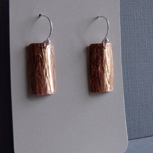 May include: A pair of copper earrings with a hammered texture and silver hooks.