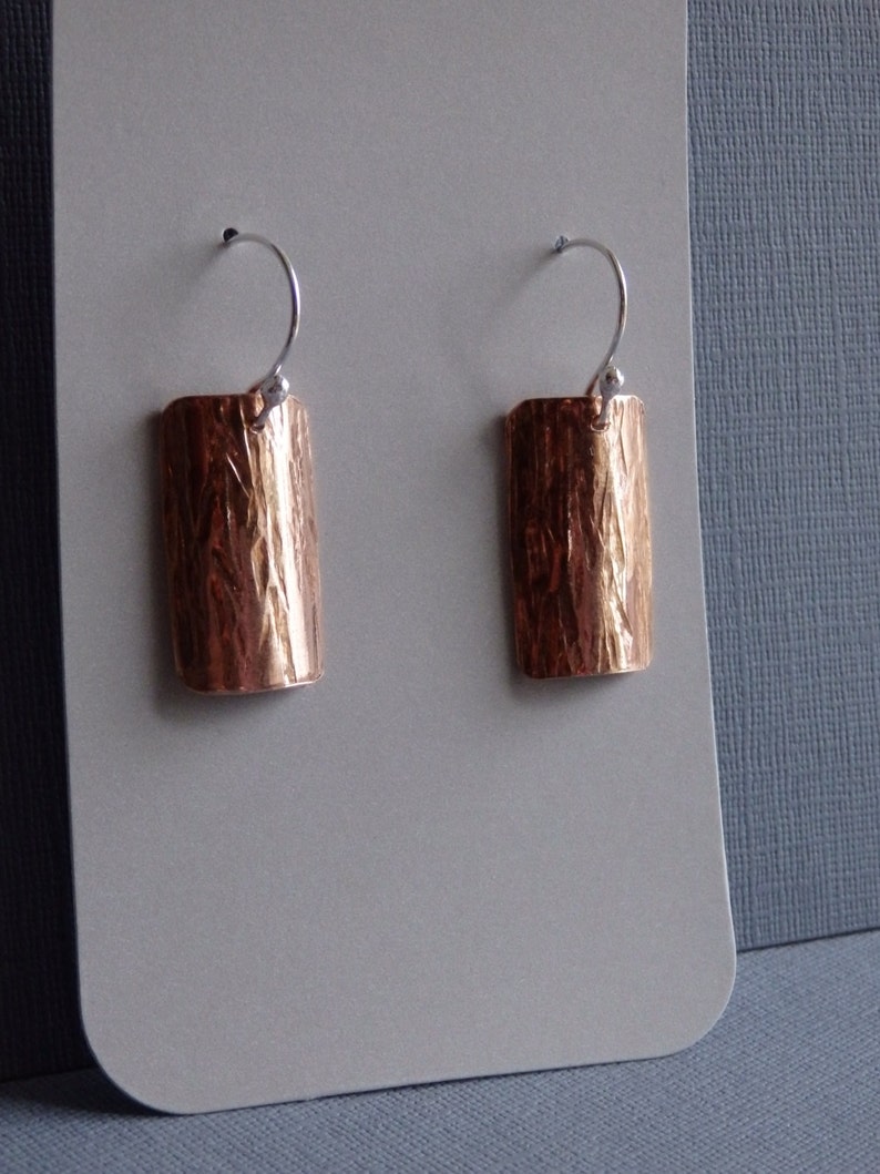 May include: A pair of copper earrings with a hammered texture and silver hooks.