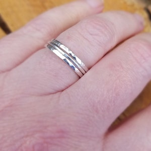 May include: Three silver hammered stacking rings worn on a finger.