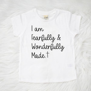 May include: White short-sleeved t-shirt with black text that reads "I am fearfully & wonderfully made. +"