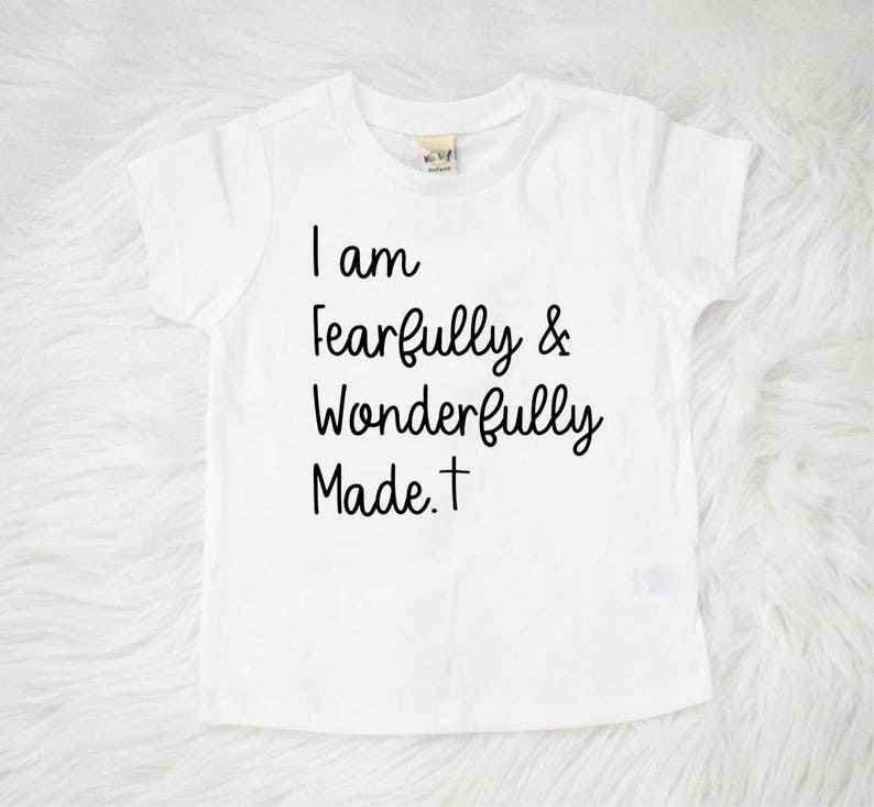 May include: White short-sleeved t-shirt with black text that reads "I am fearfully & wonderfully made. +"