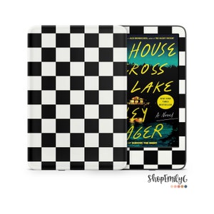 May include: A black and white checkered Kindle Paperwhite e-reader case with a book cover showing a lake scene and the text "House Across Lake" by Alex Michaelides.