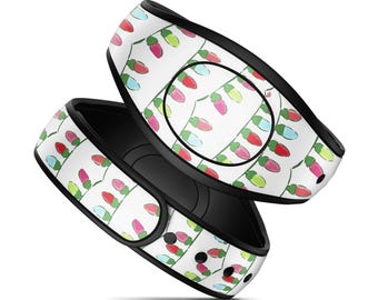 Op de afbeelding: Een witte polsband met een herhalend patroon van kleurrijke kerstlampjes in tinten rood, roze, groen en lichtblauw. De band heeft een zwarte binnenvoering en een zwart cirkelvormig middendeel met een glad en gebogen ontwerp.