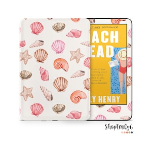May include: An e-reader device featuring a protective cover with a repeating watercolor pattern of pink and tan seashells and starfish. The screen displays the book cover for Beach Read by Emily Henry, showing a person reading on a blue towel.