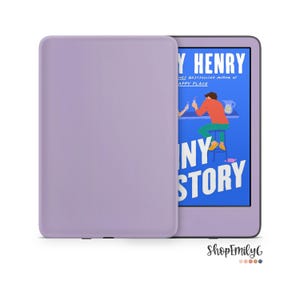 以下が含まれることがあります： 滑らかな仕上げのラベンダー色の電子書籍リーダーケース。エミリー・ヘンリー著「Funny Story」のブックカバーを表示した電子書籍リーダーの横に配置されており、明るい青色の背景にバーに座る人物のイラストが描かれています。
