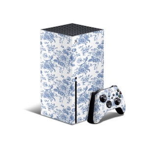 May include: A white Xbox Series X console with a blue and white floral pattern skin. The console is next to a matching blue and white floral pattern Xbox controller.