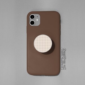May include: A brown phone case with a white and tan checkered PopSocket attached. The phone case has a dual-lens camera and is set against a gray background. The text "SHOPEMILYTG" is visible on the right side.