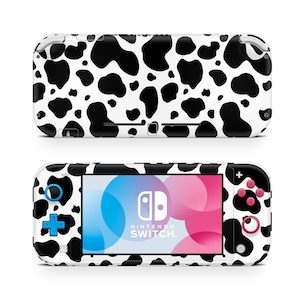 May include: A white and black cow print Nintendo Switch Lite console with a blue and pink screen. The console has a blue plus button, a pink circle button, and a black Nintendo Switch logo.