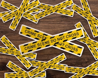 May include: A collection of rectangular stickers featuring a yellow background with black diagonal stripes and the text CRIME SCENE DO NOT CROSS printed in bold black capital letters. The stickers are arranged in a scattered, overlapping pattern.