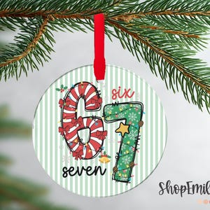 May include: Round Christmas ornament with a red ribbon. The ornament displays the numbers "6" and "7" in festive designs. The number "6" is candy cane-themed, and the number "7" is decorated with lights and a star. The words "six" and "seven" are also included.