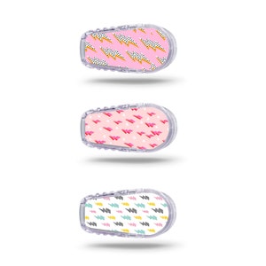 Könnte beinhalten: Drei verschiedene Designs von Klebeaufklebern für ein medizinisches Gerät. Die Aufkleber sind rosa, weiß und blau mit geometrischen Mustern.