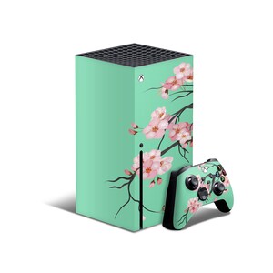 May include: A mint green gaming console with a floral design featuring pink cherry blossoms. The console is paired with a matching black and mint green controller.