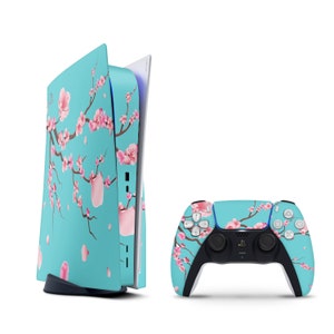 Puede incluir: Una consola PlayStation 5 azul turquesa con un diseño de flor de cerezo rosa y blanco. La consola se muestra con un mando a juego.