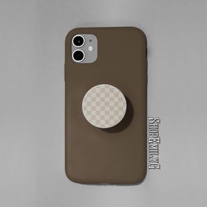 May include: A brown phone case with a matching checkered pop socket. The phone case has a dual-lens camera and the pop socket is a light beige and white checkered pattern. The text "SHOPEMILYTG" is on the right side of the phone case.