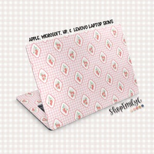 May include: A laptop skin featuring a pink gingham pattern with diamond-shaped frames containing strawberry illustrations. The text "APPLE, MICROSOFT, HP, & LENOVO LAPTOP SKINS" is printed at the top. The ShopEmilyG logo is visible.