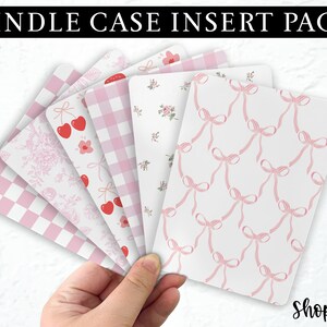 Op de afbeelding: Een set van zes roze en witte gepatroneerde papieren inlegvelletjes voor een Kindle-hoes. De patronen omvatten ruitjes, bloemen, kersen en strikken.