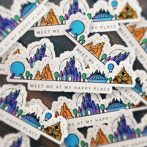 以下が含まれることがあります： 青い城、オレンジ色の山、青い球体が描かれたカラフルなテーマパークのスカイラインのイラストが特徴のダイカットステッカーのコレクション。下端には「MEET ME AT MY HAPPY PLACE」というテキストが黒い大文字で印刷されています。