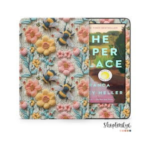 May include: A Kindle Paperwhite e-reader with a floral and bee embroidered case. The case is cream colored with pink, yellow, and blue flowers and bees. The screen shows the cover of the book "The House in the Cerulean Sea" by T.J. Klune.