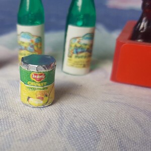 May include: A miniature can of Heinz Chunky Tomato Soup with a green and yellow label. The can is sitting on a white surface with other miniature bottles.