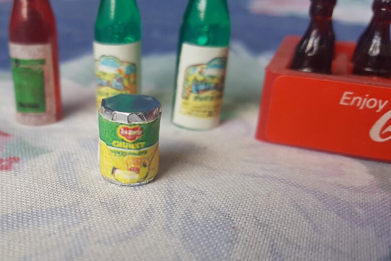 May include: A miniature can of Heinz Chunky Tomato Soup with a green and yellow label. The can is sitting on a white surface with other miniature bottles.