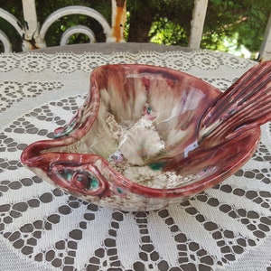 May include: A ceramic dish shaped like a fish with a red, white and green glaze. The dish has a textured surface and a raised fin.