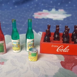 May include: A miniature set of toy bottles, including two green glass bottles, one red glass bottle, and a six-pack of brown glass bottles in a red cardboard box with the text "Enjoy Cola".