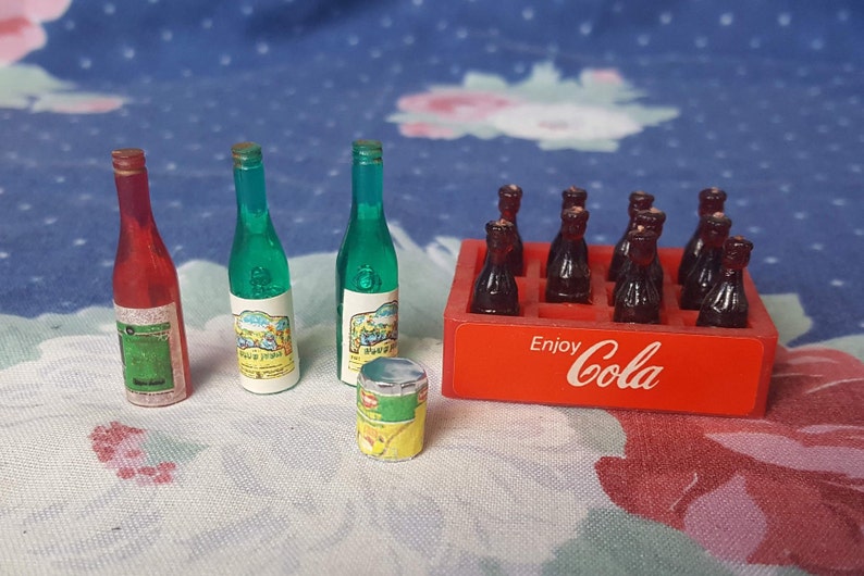May include: A miniature set of toy bottles, including two green glass bottles, one red glass bottle, and a six-pack of brown glass bottles in a red cardboard box with the text "Enjoy Cola".