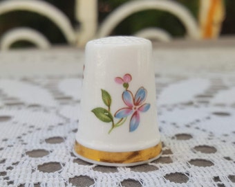 Peut inclure: Dé à coudre en porcelaine blanche avec une bordure dorée et un motif floral avec des fleurs bleues et roses.