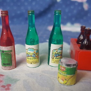 May include: A miniature set of toy bottles, including two green glass wine bottles with labels, a red glass wine bottle with a label, and a six-pack of brown glass soda bottles in a red and white cardboard box with the word "Enjoy" printed on it. There is also a small green and yellow can with a label.