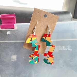Peut inclure: Boucles d'oreilles pendantes avec les chiffres "43" dans un motif coloré rouge, jaune, vert et bleu. Les boucles d'oreilles sont fixées à des crochets d'oreille argentés et présentées sur une carte marron.