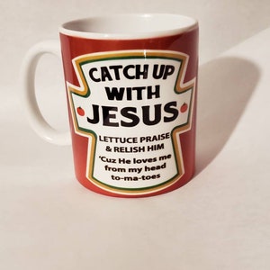 May include: Red ceramic mug with a white handle. The mug has a ketchup-style label that says "Catch Up With Jesus." The label also says "Lettuce Praise & Relish Him 'Cuz He loves me from my head to-ma-toes."