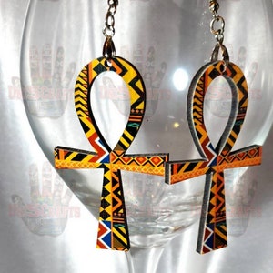 May include: A pair of wooden earrings shaped like the Ankh symbol, a cross with a loop at the top. The earrings are decorated with a colorful geometric pattern in shades of yellow, orange, red, blue, and black.