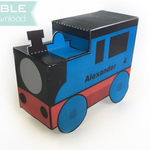 May include: A blue, red, and black train-shaped box with the name "Alexander" and the number "4" printed on the side. The box has a black top and a large gray circle on the front, resembling a train's face. The text "EDITABLE Instant Download" is in the upper left corner.