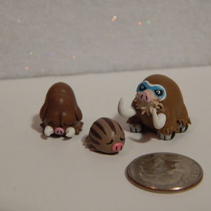 May include: Three handmade clay figurines of brown and white woolly mammoths. The largest mammoth has a blue eye mask.