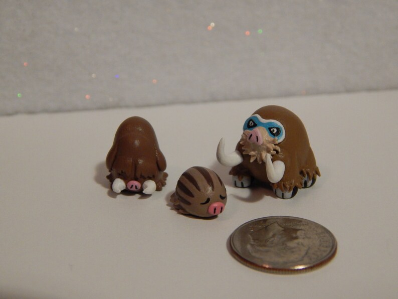 May include: Three handmade clay figurines of brown and white woolly mammoths. The largest mammoth has a blue eye mask.