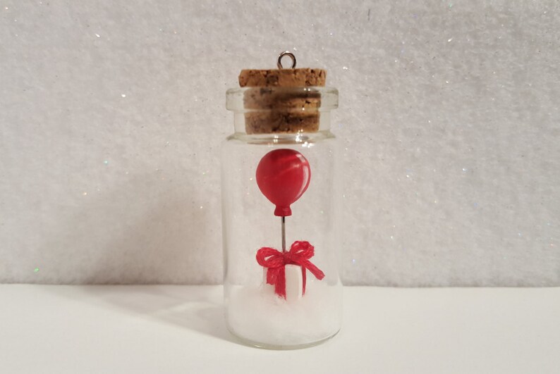 Peut inclure: Une petite bouteille en verre avec un bouchon en li&egrave;ge contient un ballon rouge attach&eacute; &agrave; une bo&icirc;te cadeau blanche avec un ruban rouge. La bouteille est remplie de paillettes blanches.