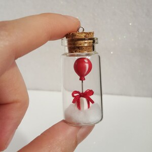 Peut inclure: Une petite bouteille en verre avec un bouchon en li&egrave;ge contient un ballon rouge miniature, une bo&icirc;te cadeau blanche avec un ruban rouge et du coton blanc. La bouteille a une boucle argent&eacute;e en haut pour l'accrocher.