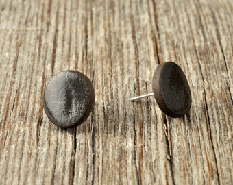 Könnte beinhalten: Ein Paar schwarze Keramik-Ohrstecker. Die Ohrringe sind rund und haben eine glatte, glänzende Oberfläche.