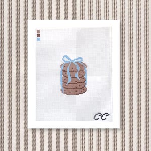 May include: A needlepoint design of a stack of brown cookies tied with a light blue ribbon. The cookies are in a stack, and the ribbon is tied in a bow. The background is white, and the image is on a white canvas.