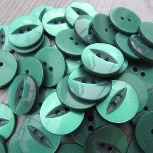 May include: A pile of green plastic buttons with two holes. Some buttons have a decorative groove.